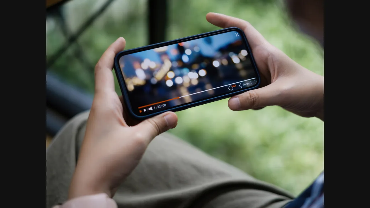 Hands holding a phone sideways playing a video, with playback controls visible