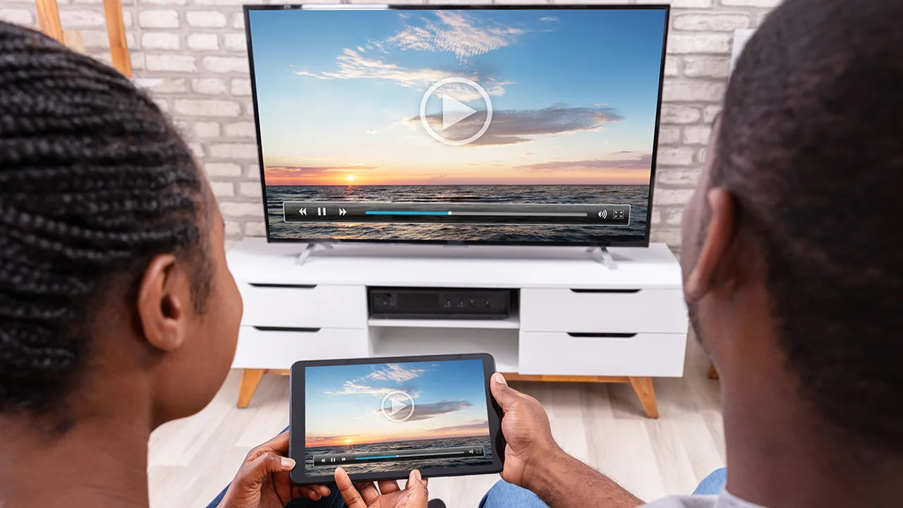 Couple watching the same sunset video on a large TV and on a tablet, both showing player controls