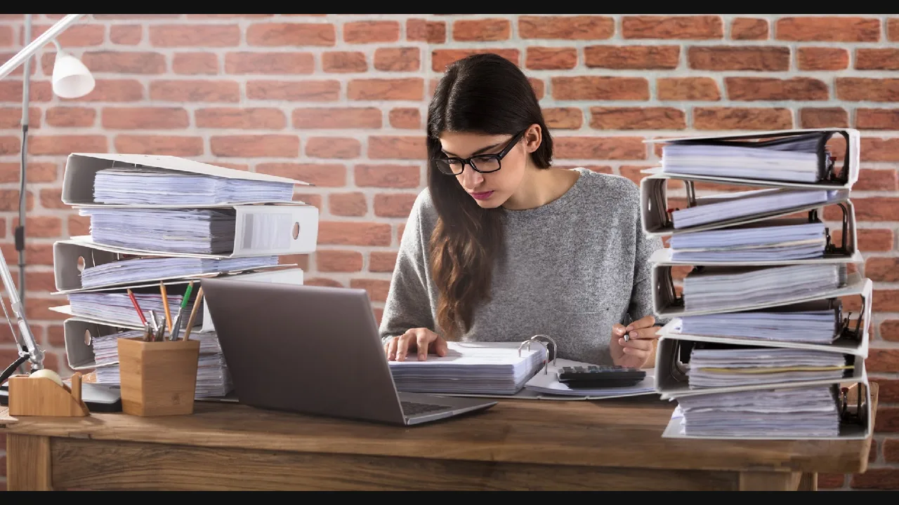 Woman sorting folders and binders at a desk with a laptop